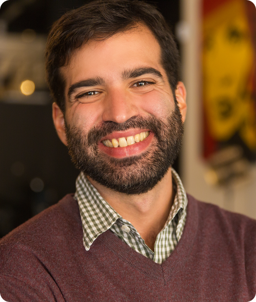 Man with brown sweater and beard smiling warmly indoors